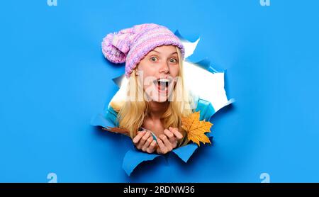 Überraschte Frau in Strickmütze mit Herbstblättern, die durch das Papierloch blickten. Herbstverkäufe. Rabatt. Saisonverkäufe. Erstauntes Mädchen im trendigen Herbst Stockfoto