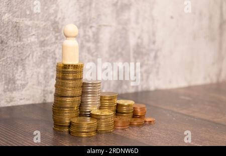 Miniaturmenschen: Geschäftsmann-Figur hebt die Hand und hält eine Tasche, die auf einem Goldmünzstapel steht. Geld-, Investitions- und Finanzkonzepte. Stockfoto