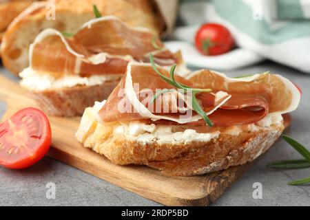 Leckere Sandwiches mit geräuchertem Schinken, Tomaten und Rosmarin auf grauem Tisch, Nahaufnahme Stockfoto