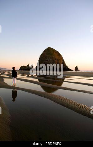 Eine Frau, die die Landschaft am Haystack Rock und die Gezeitenpools am Cannon Beach, OR, genießt Stockfoto