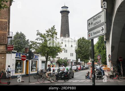 Köln, Deutschland. 21. Juli 2023. Fußgänger und Radfahrer vor dem Leuchtturm in Köln Ehrenfeld. Der einzige Leuchtturm Nordrhein-Westfalen steht im Kölner Ehrenfeld. Es hat keinen Zweck. Es ist einfach da - und vielleicht ist es deshalb so beliebt. Der bekannteste Ehrenfelder kämpft jetzt für eine Wiederbelebung. (Zu dpa/lnw: 'Der Leuchtturm von Köln-Ehrenfeld - ohne Bedeutung und doch geliebt') Kredit: Oliver Berg/dpa/Alamy Live News Stockfoto