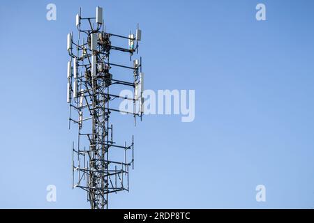 Hoher monopoler Zellenturm mit Metallgerüst und Antennen – graue rechteckige Paneele – blauer Himmelshintergrund Stockfoto