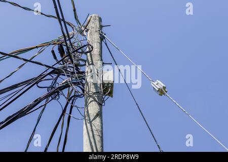 Hölzerne Stange mit verwickelten Drähten und Kabeln am blauen Himmel Stockfoto