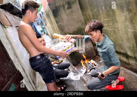 Junge vietnamesische Männer verbrennen Opfergaben oder Spaßpapiere oder Geisterpapiere für einen Freund namens Thành Kot, der im Alter von 20 Jahren gestorben war. Joss Papiere sind Papiere mit bestimmten Mustern, Farben und Symbolen, um Wertgegenstände wie Geld, Gold, Häuser und Autos zu imitieren. Man geht davon aus, dass die Tat, sie zu verbrennen, eine Verbindung zum Jenseits herstellt und die Opfer an die verstorbenen Familienmitglieder sendet. Die Leute glauben, dass der Verstorbene durch dieses Ritual ein besseres Leben führen wird. Stockfoto