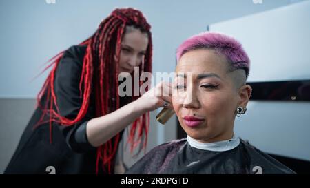 Friseur schneidet asiatische Frau mit kurzen rosa Haaren im Friseursalon. Stockfoto