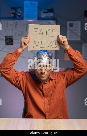 Ein seltsamer Mann mit Schutzfolie und Brille, der ein Banner mit gefälschter Nachricht hält. Verschwörungstheorie und falsche Nachrichten Stockfoto