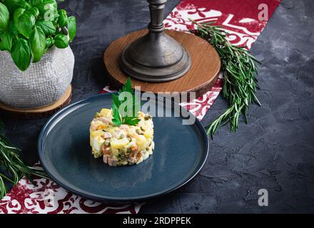 Salat mit Petersilie, Olivier, in einer schwarzen Schüssel auf dem Tisch, selektiver Fokus. Traditioneller russischer Salat mit Kopierbereich. Stockfoto