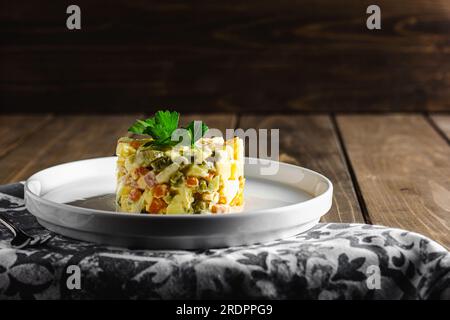 Traditioneller russischer Salat Olivier aus gekochtem Gemüse und Wurst mit Mayonnaise in der Schüssel. Russischer Neujahrssalat oder Weihnachtssalat auf Holzhintergrund Stockfoto