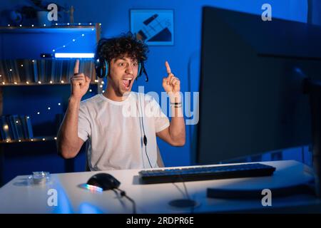 Ein überraschter junger arabischer Gamer, der Kopfhörer trägt, Videospiele auf dem PC spielt, mit einem schockierten Gesicht in die Kamera schaut, im eSport-Cyber spielt Stockfoto