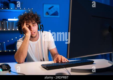 Ein arabischer Gamer in einem Headset schläft nachts in einem Spielesessel in der Nähe des Computers. Nächtliches Training. Stockfoto