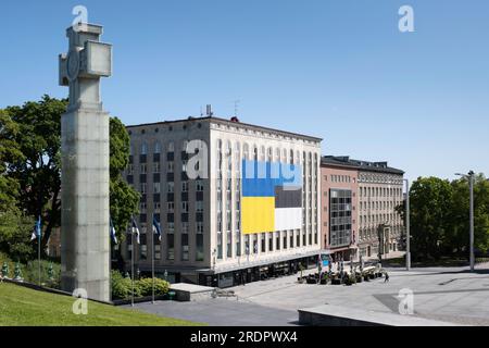 Riesige gelbe blaue Flagge der Ukraine an der Fassade eines Gebäudes auf dem Freiheitsplatz mit links vom Kreuz der Freiheit in Tallinn Stockfoto