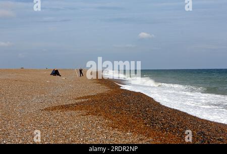Ein Seeangler am Kiesstrand mit moderater See an einem windigen Tag im Sommer in North Norfolk in Cley Next the Sea, Norfolk, England, Großbritannien. Stockfoto