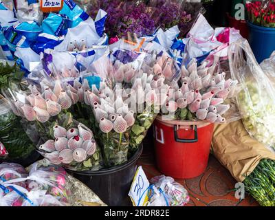 Auf dem belebten Blumenmarkt von Bangkok, Thailand, heben sich die leuchtenden roten Rosen hervor, wenn sie verpackt und zum Verkauf vorbereitet werden, was potenzielle Käufer verlockt Stockfoto