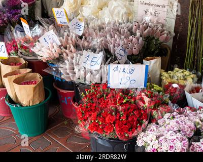 Eine vielfältige Auswahl an lebendigen Blumen, geschmückt mit Preisschildern, lockt Kunden auf dem geschäftigen Blumenmarkt von Bangkok, Thailand. Stockfoto