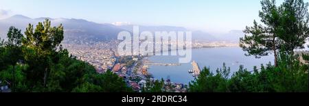 Genießen Sie den atemberaubenden Blick auf Alanya von der Aussichtsplattform mit üppigen Bäumen, blauem Meer und dem berühmten Leuchtturm und Hafen von Alanya. Die felsigen Stifte Stockfoto