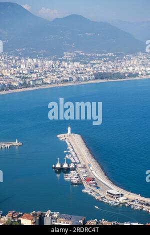 Genießen Sie den atemberaubenden Blick auf Alanya von der Aussichtsplattform mit üppigen Bäumen, blauem Meer und dem berühmten Leuchtturm und Hafen von Alanya. Die felsigen Stifte Stockfoto