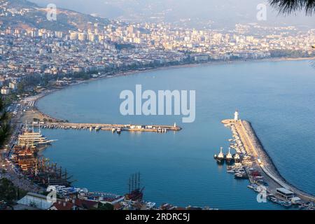 Genießen Sie den atemberaubenden Blick auf Alanya von der Aussichtsplattform mit üppigen Bäumen, blauem Meer und dem berühmten Leuchtturm und Hafen von Alanya. Die felsigen Stifte Stockfoto