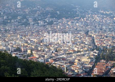 Genießen Sie den atemberaubenden Blick auf Alanya von der Aussichtsplattform mit üppigen Bäumen, blauem Meer und dem berühmten Leuchtturm und Hafen von Alanya. Die felsigen Stifte Stockfoto