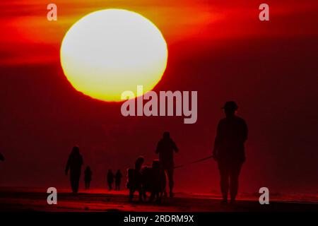 Isle Of Palms, Usa. 23. Juli 2023. Die Menschen, die sich vor einem dramatischen Sonnenaufgang abschotten, machen einen frühen Morgenspaziergang am Strand am 23. Juli 2023 auf der Isle of Palms, South Carolina. Eine anhaltende Hitzewelle über den Süden der USA bringt weiterhin extrem heißes, feuchtes Wetter in die Region. Kredit: Richard Ellis/Richard Ellis/Alamy Live News Stockfoto