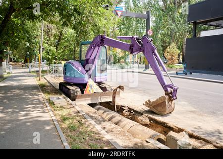 Bohrstraße für große Presslufthammer. Schwere Maschinen zerkleinern Asphalt für die Reparatur von Regenwasserabflüssen. Hydraulikbagger läuft im Wasser. Reparatur und Erweiterung Stockfoto