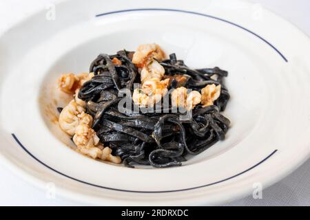 Serviert wird eine Portion italienischer Tintenfisch-Pasta mit Garnelen, serviert auf weißem Teller Stockfoto