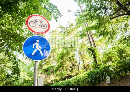 Fahrrad- und Fußgängerschilder im Sommer. Italien. Blick auf ein generisches Schild „Fahrradrennen verboten“ auf einem Fußgängerweg. Das „kein Radfahren“-Zeichen bedeutet, dass die Verwendung von verwendet wird Stockfoto