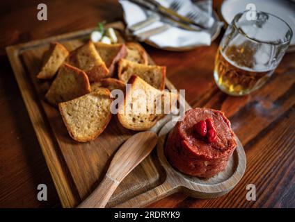 Holztisch mit Tartar Steak und Toast an Bord, Teller, Besteck und Bier. Stockfoto