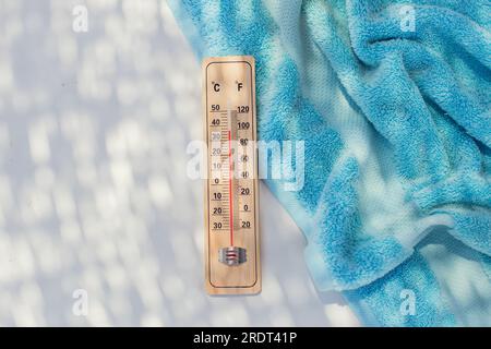 Thermometer und Handtuch auf weißem Hintergrund. Sommer-, Hitze- und Urlaubskonzept Stockfoto