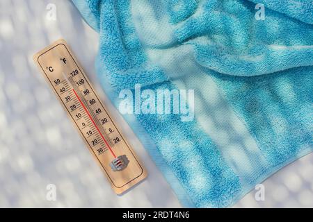 Thermometer und Handtuch auf weißem Hintergrund. Sommer-, Hitze- und Urlaubskonzept Stockfoto