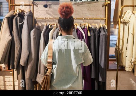 Rückansicht einer jungen schwarzen Frau, die Kleidung in Kleiderständern durchsucht, in einer Modeboutique, Kopierraum Stockfoto