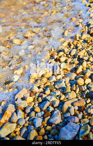 Wasser fließt über kleine Felsen und Steine am Ufer eines Teichs oder Sees Stockfoto
