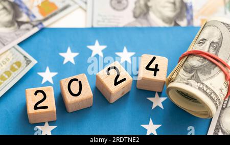 2024-Inschrift auf Holzwürfeln auf der Konsistenz von US-Dollar- und Euro-Banknoten Stockfoto