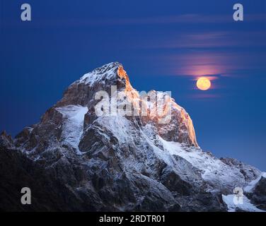 Berggipfel bei Sonnenaufgang. Berg Ushba, Svaneti, Georgien, Kaukasus. Die ersten Sonnenstrahlen. Vollmond über den Kamm Stockfoto