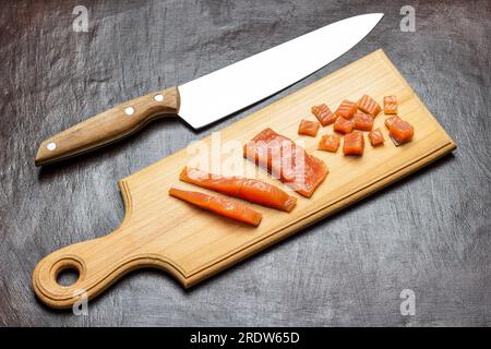 Lachs in Scheiben auf dem Schneidebrett. Küchenmesser auf dem Tisch. Speicherplatz kopieren. Draufsicht. Brauner Hintergrund. Stockfoto
