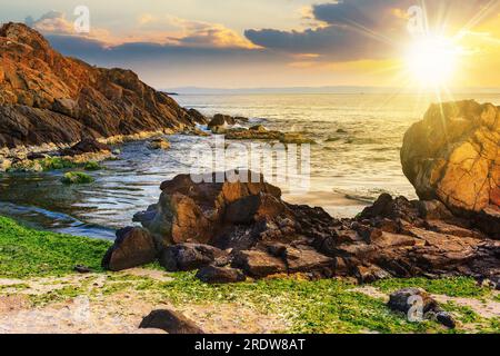 Anzahl der Steine und Felsen an der sandigen Küste bei Sonnenuntergang. Algen lagen auf dem Sand und machten ​​by den Sturm im Abendlicht Stockfoto