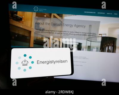 Person, die ein Smartphone mit dem Logo der dänischen Energieagentur Energistyrelsen auf dem Bildschirm vor der Website hält. Konzentrieren Sie sich auf das Display des Telefons. Stockfoto