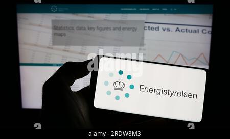 Person, die ein Mobiltelefon mit dem Logo der dänischen Energieagentur Energistyrelsen auf dem Bildschirm vor der Webseite hält. Konzentrieren Sie sich auf das Display des Telefons. Stockfoto