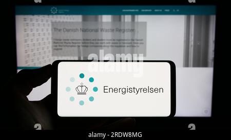 Person, die ein Mobiltelefon mit dem Logo der dänischen Energieagentur Energistyrelsen auf dem Bildschirm vor der Webseite hält. Konzentrieren Sie sich auf das Display des Telefons. Stockfoto