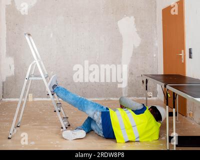 Ein Helmarbeiter ist von einer Arbeitsleiter gefallen. Sicherheitskonzert. Stockfoto