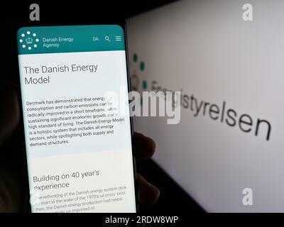 Person, die ein Mobiltelefon mit der Webseite der dänischen Energieagentur Energistyrelsen auf dem Bildschirm vor dem Logo hält. Konzentrieren Sie sich auf die Mitte des Telefondisplays. Stockfoto
