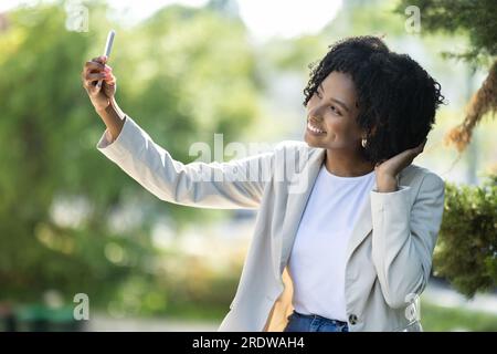 Süße, hübsche, junge schwarze Frau, die Selfie im Park macht Stockfoto