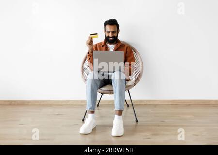 Indischer Mann mit Kreditkarte und Laptop, der an der Wand einkauft Stockfoto