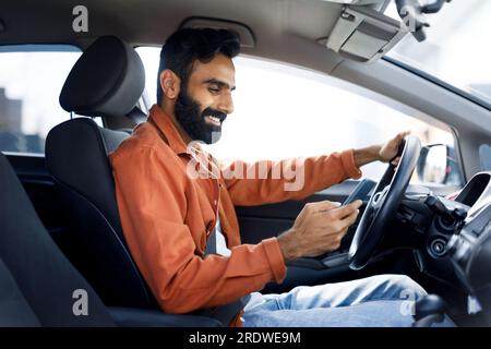Indischer Typ, der während der Autofahrt Smartphone-Nachrichten benutzt, Seitenansicht Stockfoto