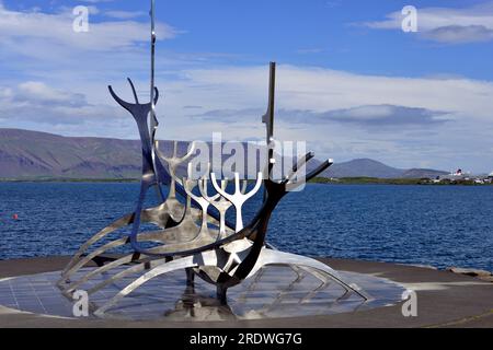 Edelstahlskulptur eines Wikingerschiffs, bekannt als Sun Voyager in Reykjavik Island. Videyjarstofa House kann man in der Ferne sehen. Stockfoto