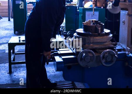 Große industrielle Dreh- und Schraubenschneidemaschine für Metall und Teile mit Ersatzteilen sowie ein Arbeiter in einem Bademantel im Werk. Stockfoto