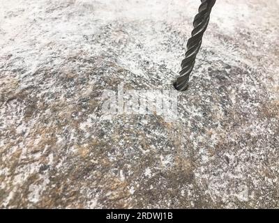 Ein robuster Hartmetallbohrer bohrt ein Loch in einen großen grauen Stein. Ansicht schließen. Der Hintergrund. Stockfoto