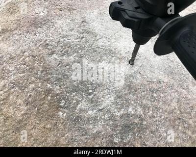 Ein robuster Hartmetallbohrer bohrt ein Loch in einen großen grauen Stein. Ansicht schließen. Der Hintergrund. Stockfoto