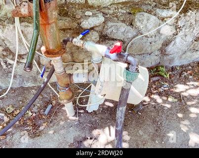 Gewinnung von Wasser aus unterirdischen Quellen. Weiße Kunststoffflaschen sind an die Ventile zum Pumpen von Wasser angeschlossen. Stockfoto