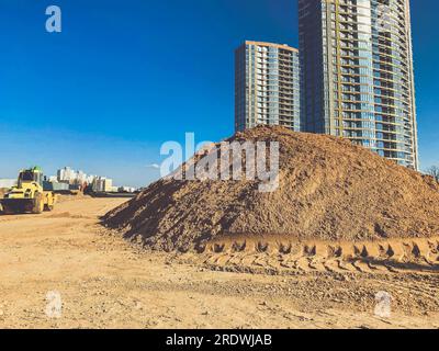 Sand auf einer Baustelle in einer neuen Nachbarschaft. Große, sandige Haufen vor der Kulisse von Häusern, die aus Blöcken und Glas errichtet wurden. Hochhaus Stockfoto