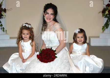 Die Braut und ihre beiden Blumenmädchen ruhen sich an ihrem Hochzeitstag auf der Kirchtreppe aus. Die Braut trägt ein Kleid mit Flügelärmeln und kleine Mädchen tragen ärmellose dr. Stockfoto